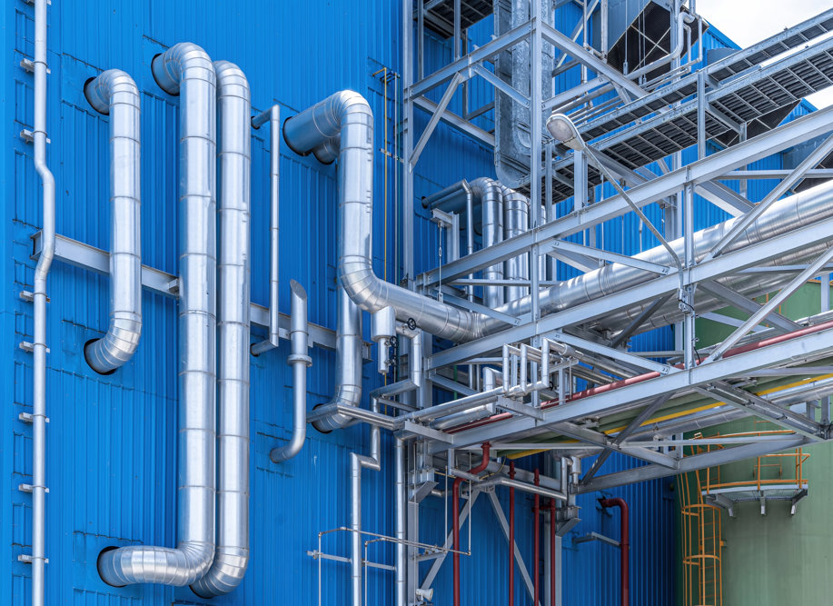 Silvriga stålrörledningar monterade mot korrugerad blå metallfasad vid industrianläggning